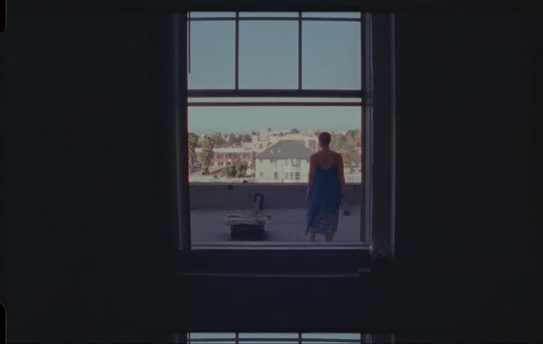 Woman climbs through window to stand looking at view of houses