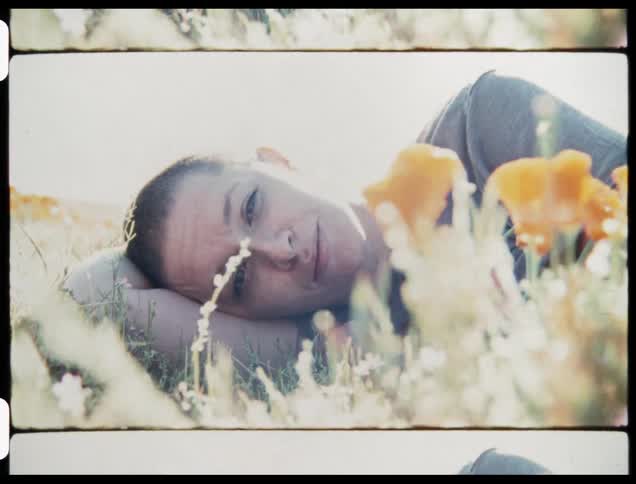 A woman laying down in a grassy field with flowers in the foreground and the sky in the background