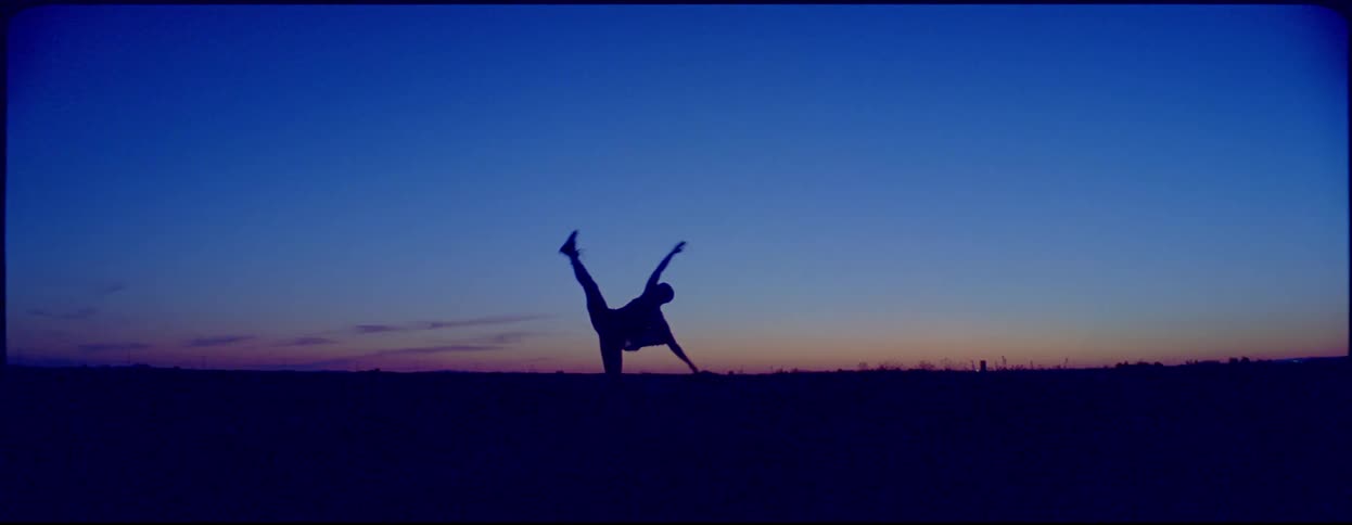 The silhouette of a woman dancing in a field under a clear sky at sunset