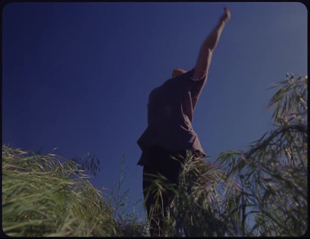 A young woman dances amongst tall grass in a field on a sunny day