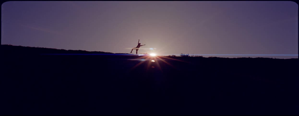 A person dances at the edge of hill as the sun rises in the morning