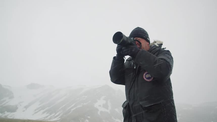 Photographer stands taking picture in snowstorm obscuring mountains in background