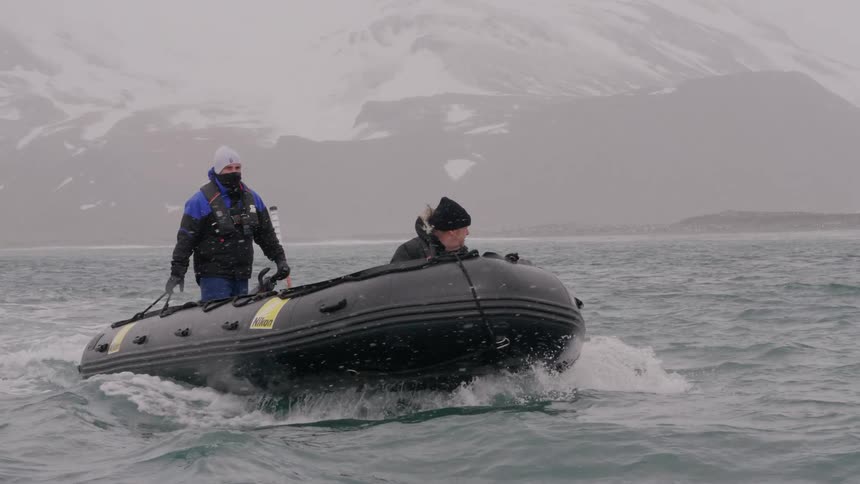 Two men on a raft in the ocean while snowing with a mountain range in the background