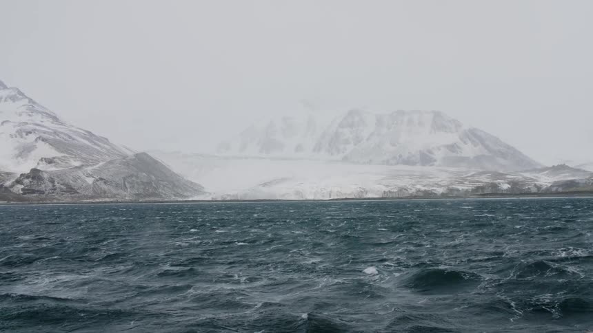 Ocean waves flowing in front of snowy mountains in the arctic