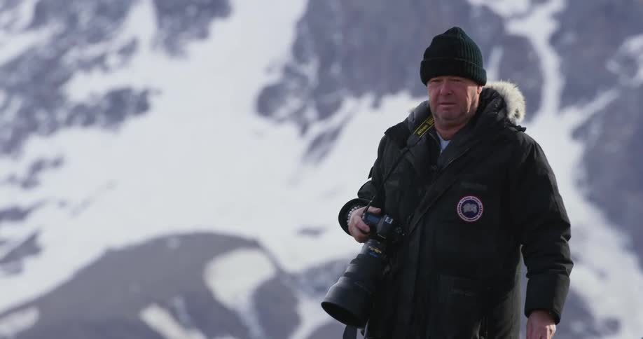 A man walking at the base of a mountain with a camera