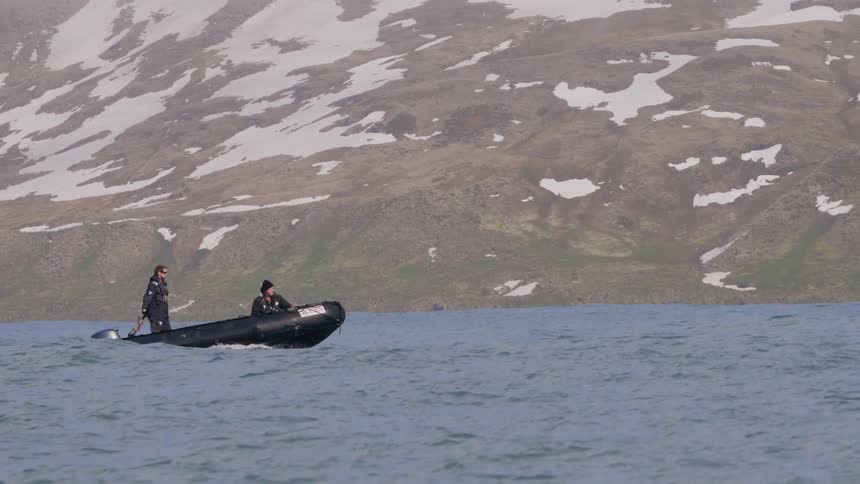 Two men on a raft on a lake with a mountain range covered in snow in the background