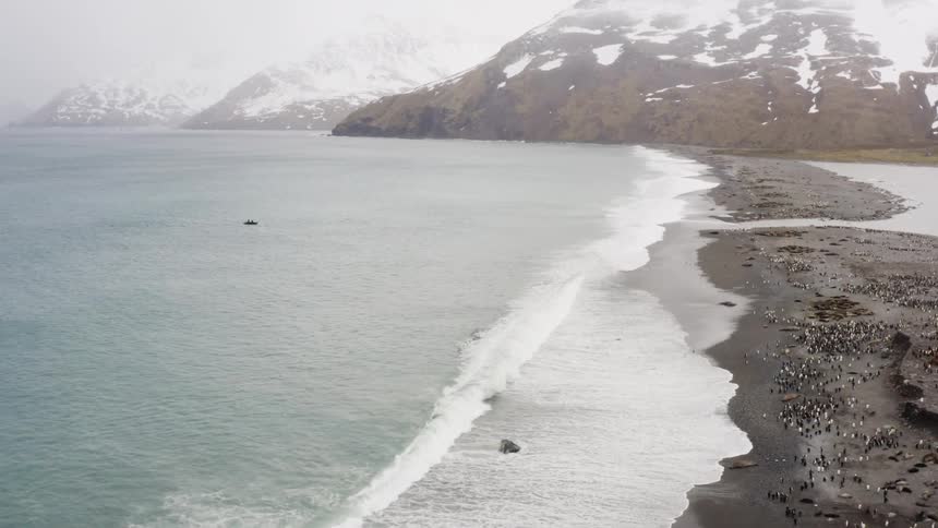 Aerial view of penguins on the shore and a boat in the water with mountains in the background