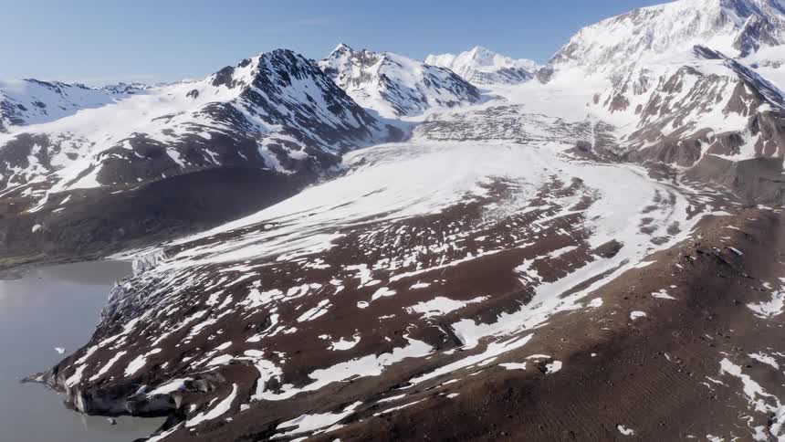 Snow covers the slopes of a mountain near a small body of water