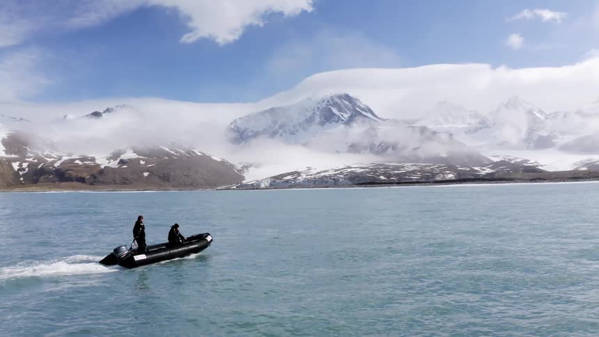 Two men boating in the water with snow covered mountains behind them