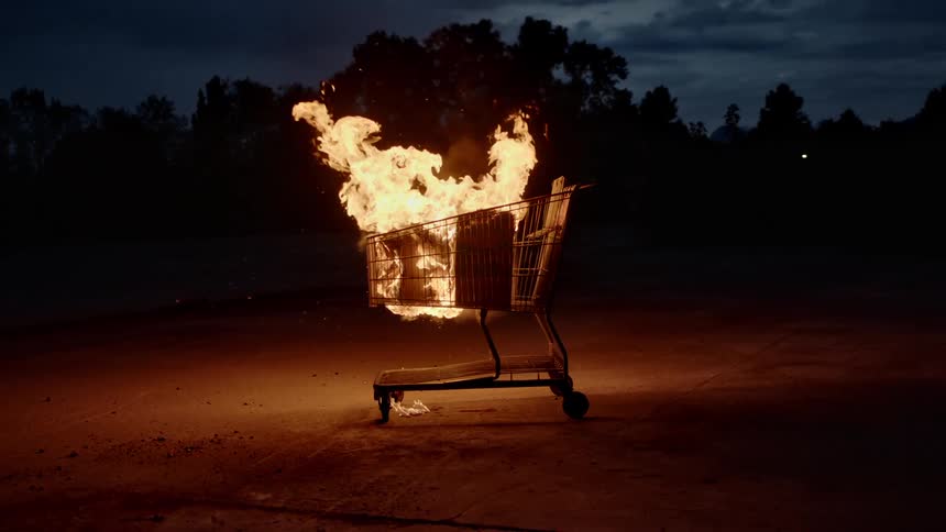 An abandoned shopping cart is engulfed in flames outdoors at nighttime