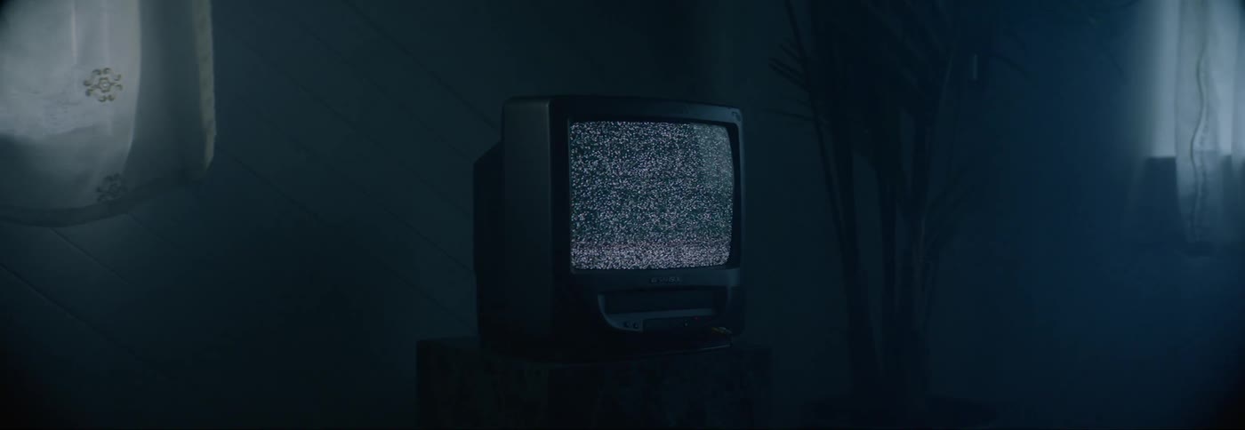 Television set over a table in a dimly lit room showing static in the screen