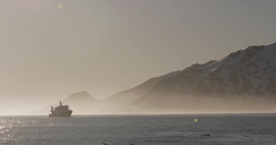 A boat on the ocean water with a mountain range and the sky in the background
