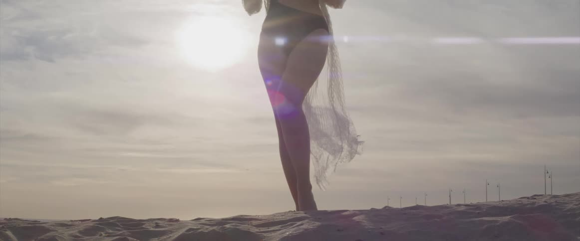 A woman with a bathing suit standing on sand with the sky and clouds in the background