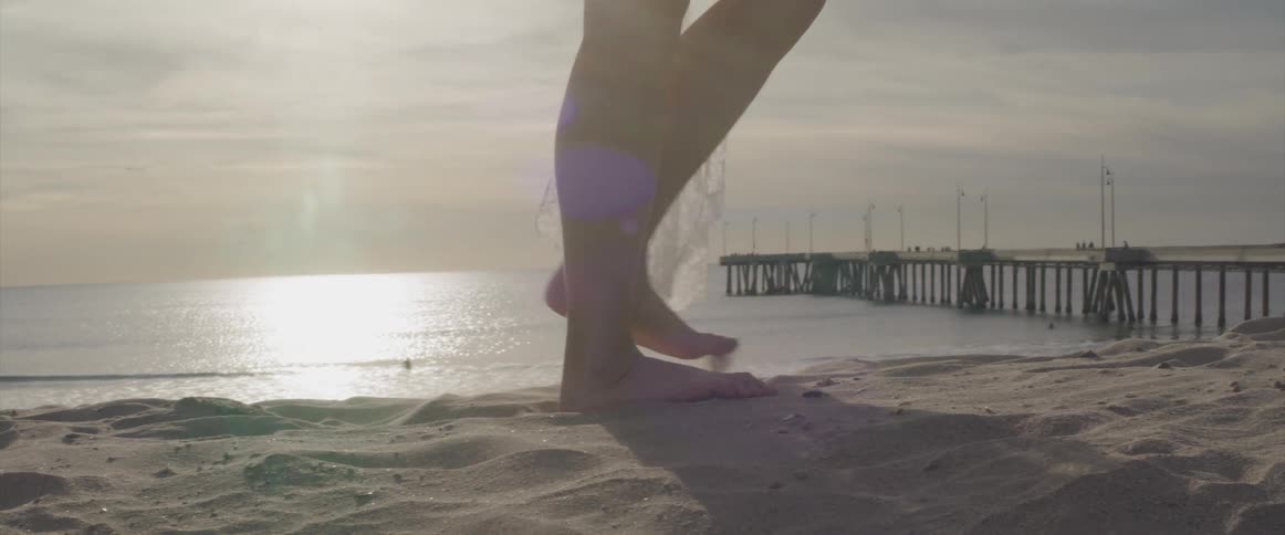A woman wearing a white lace cover up walks barefoot in the sand