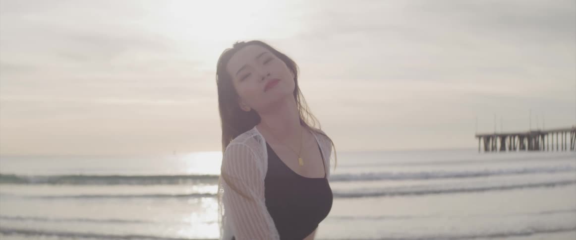 Woman modeling for the camera on the sand of a beach at sunset next to a pier