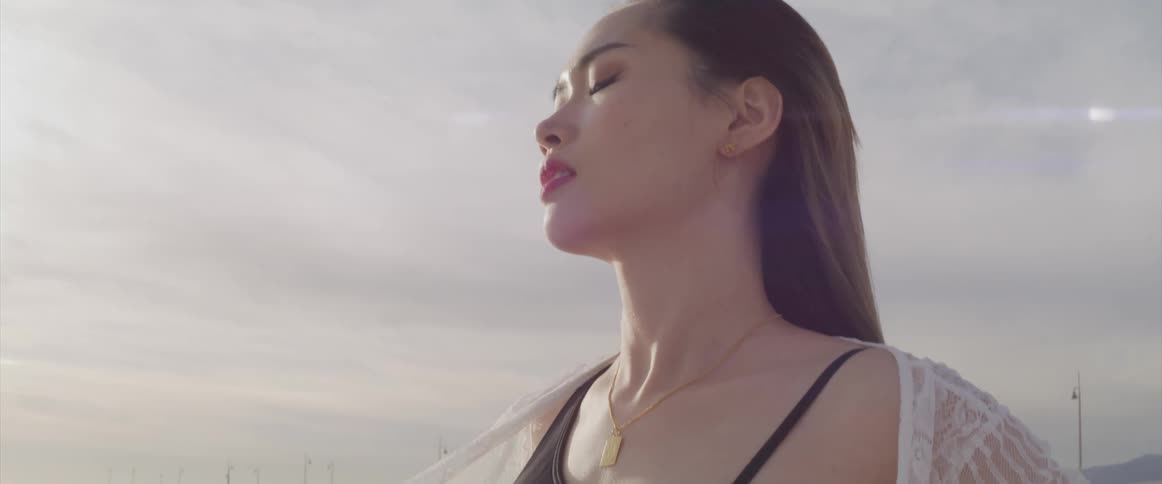 A young asian woman stands and poses on a beach in front of a long pier