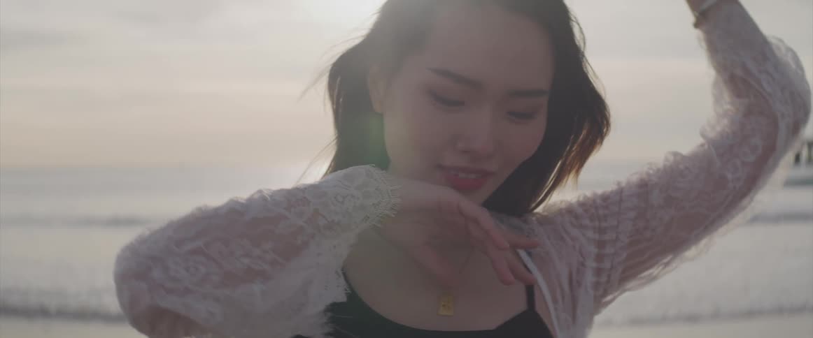 A young asian woman posing on the beach looks into the camera before twirling away