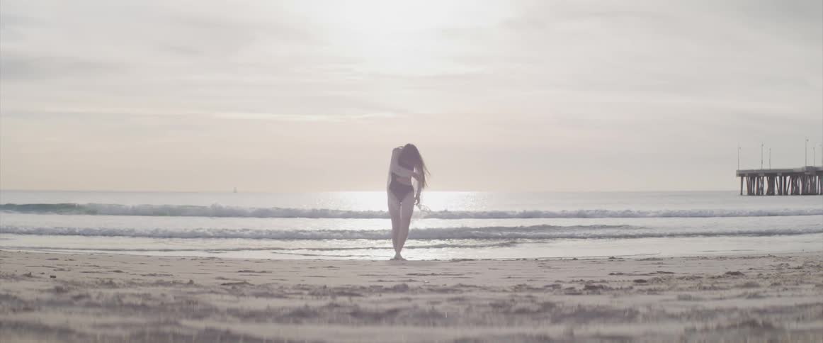 A woman dances by herself alone the ocean shoreline