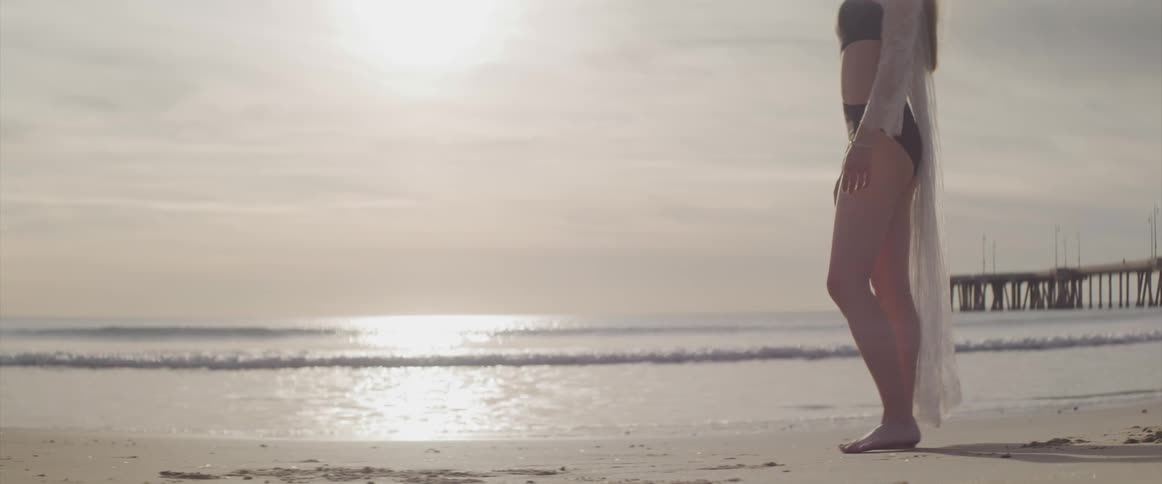 A young woman at the beach rubs her toes in the sand