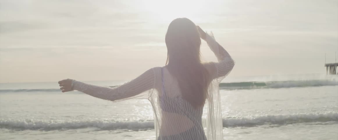Woman moves her arms on the beach at sunset next to a pier