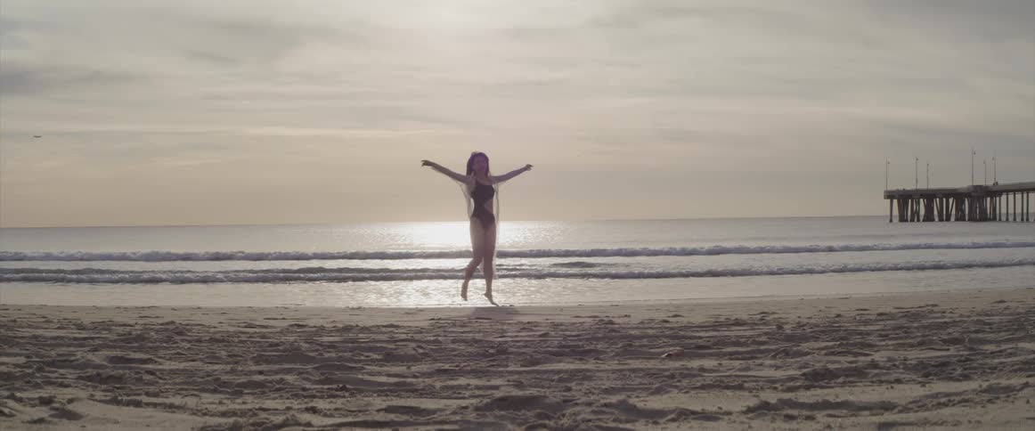 Woman wearing swimsuit and wrap stretches and move on beach