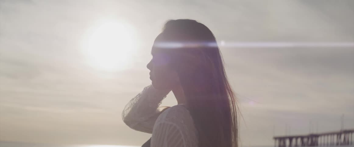 A teenage girl standing on the beach runs her hand through her hair
