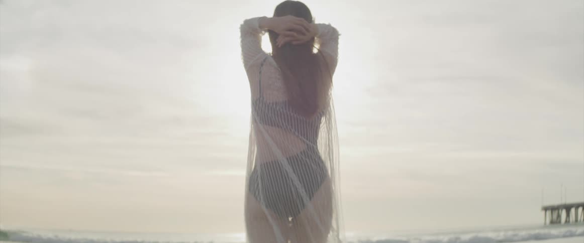 A teenage girl standing on the beach and looking out at the water
