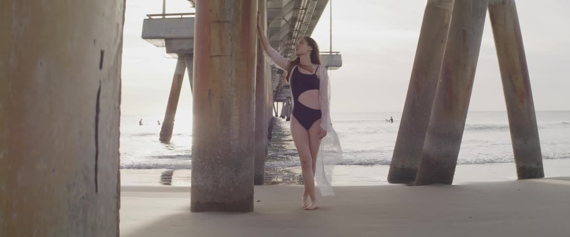 A teenage girl leans against a pier on the beach