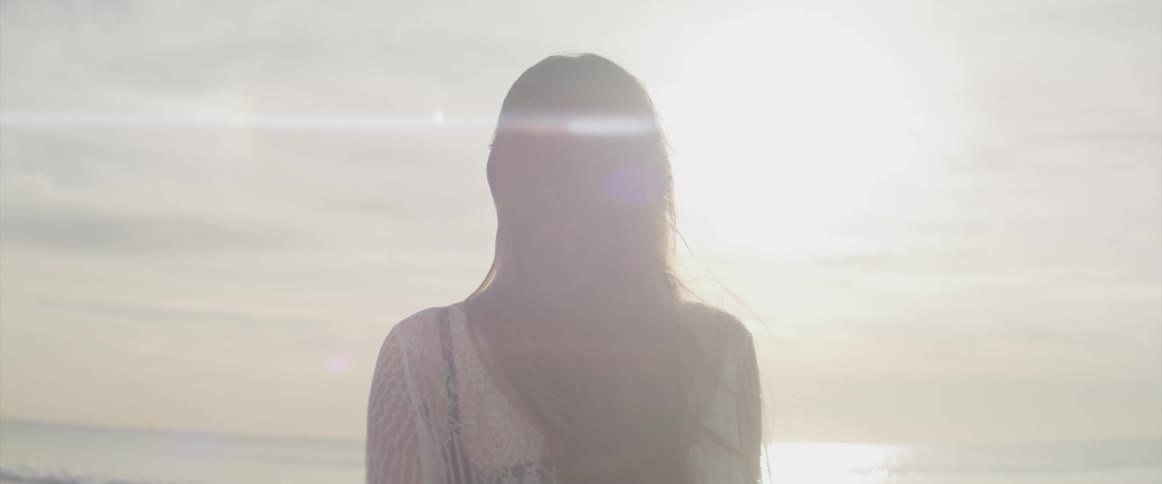 A woman standing on the beach with a pier the ocean and the sky in the background