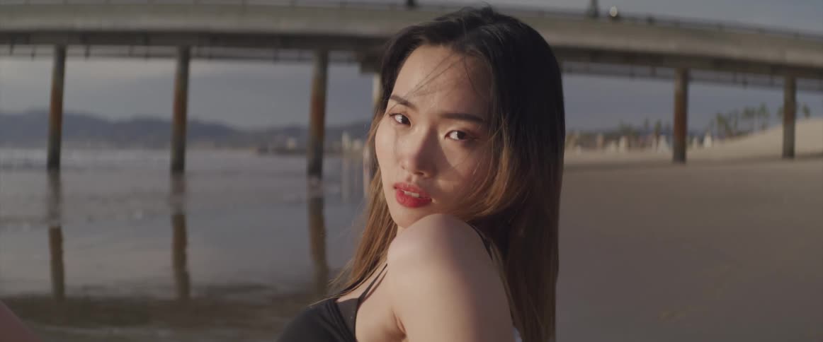A woman standing and staring on a beach with a pier in the background