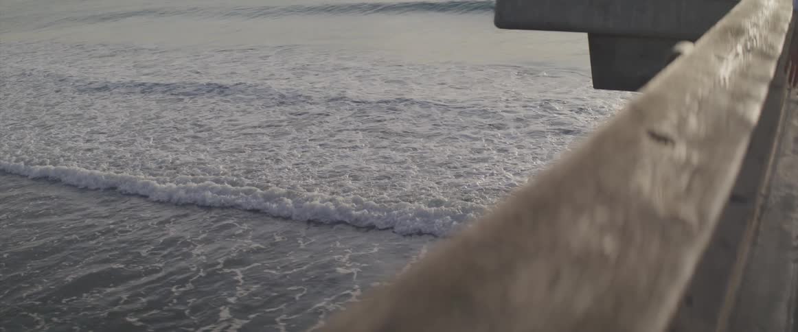 Ocean waves break against the shore seen from a pier