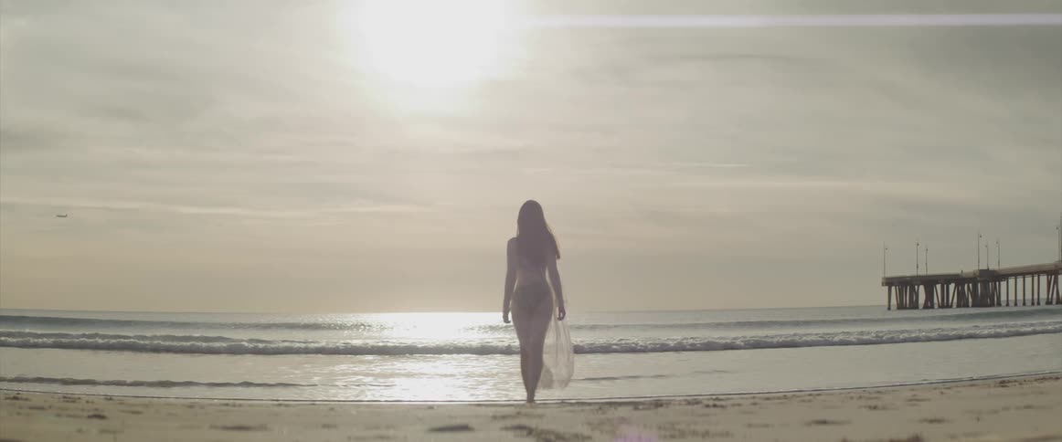 Asian woman with a black bikini and a white transparent dress walks into the sea on the beach