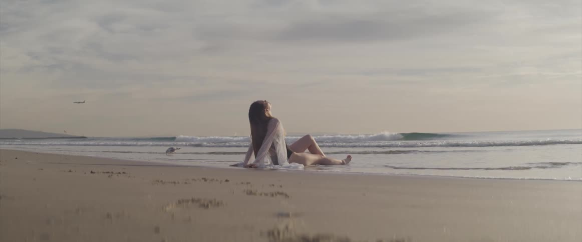 A woman sits quietly on the beach along in the shallow incoming water