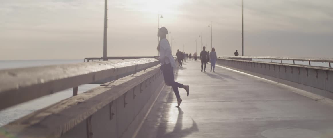A woman walks fast to the edge of the pier and pushes her self into the air from the railing