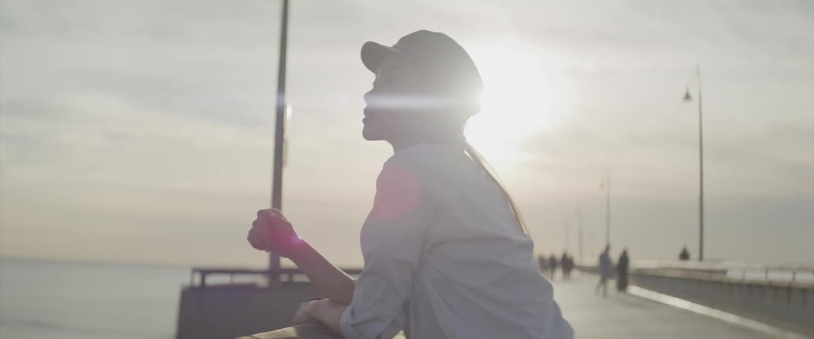 A young woman leans against the railing on a pier