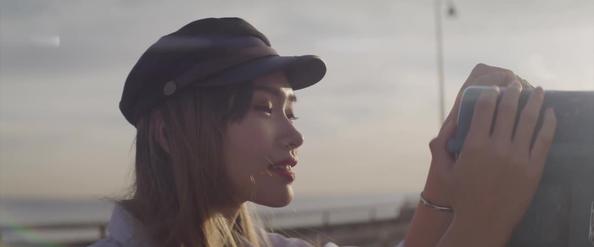 A woman is outdoors at dusk and looking through a telescope