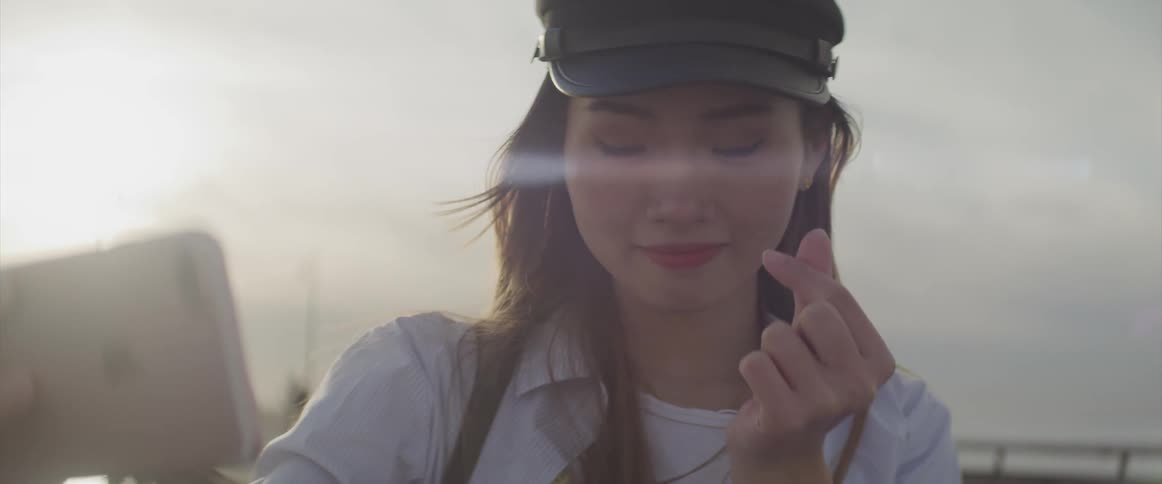 An asian female smiles as she holds her smartphone up to take a selfie