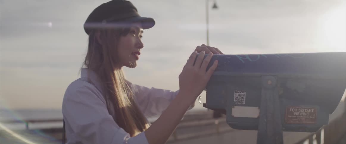 A woman holds onto a telescope viewer on a beach pier before looking through it