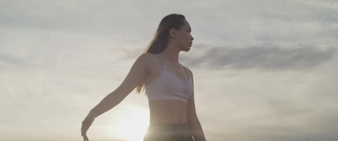 Woman exercises by doing tai chi outdoors as sun sits on horizon