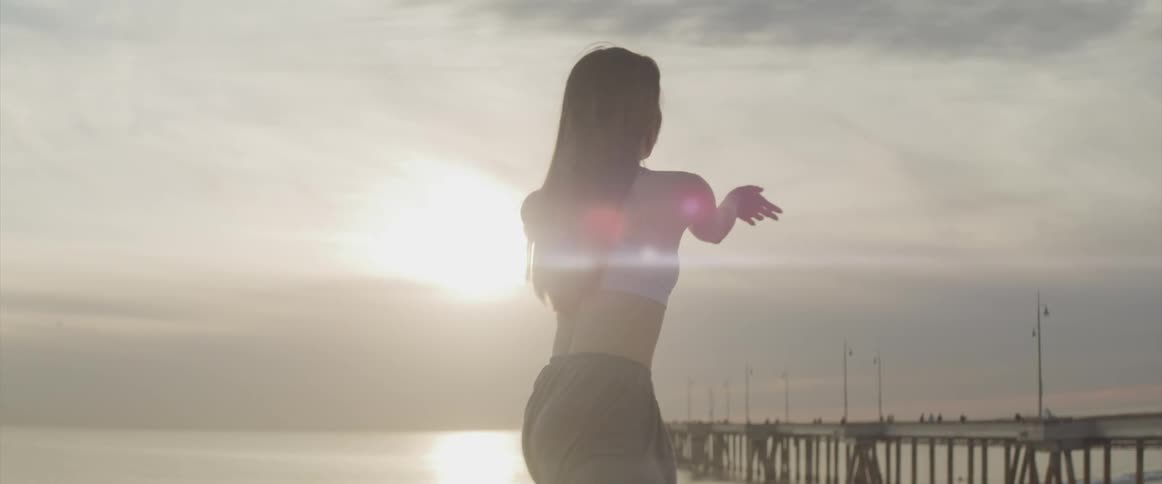 Woman exercises on the beach near a pier