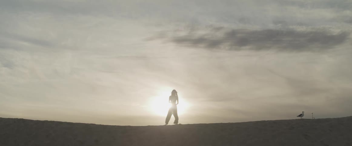A woman that is exercising is silhouetted against the sun