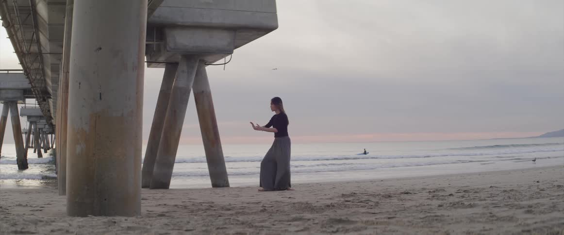A woman performs calming meditation moves standing on the beach