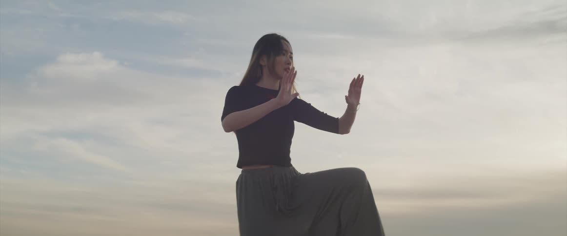 An asian woman stands on the beach and practices martial arts forms by herself
