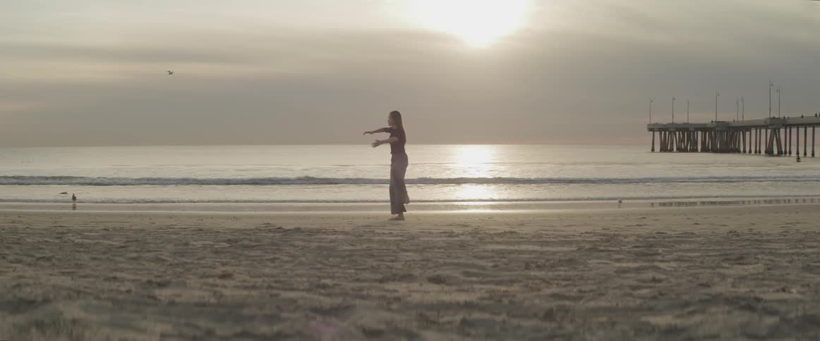 A woman does meditation stretches and moves on a sandy beach