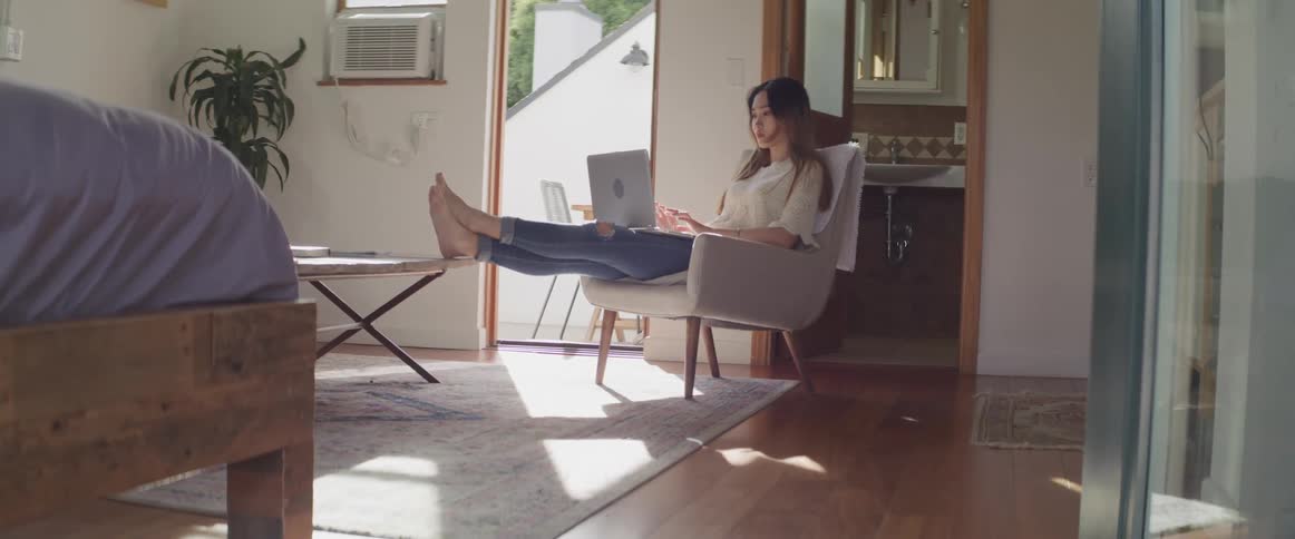 A woman sitting on a chair with her foot on a table with a laptop on her lap