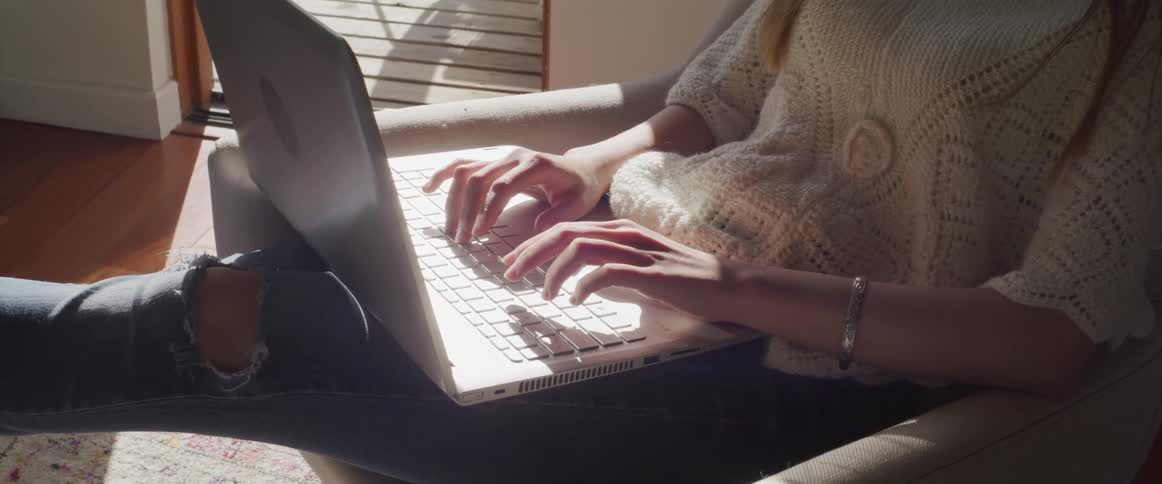 A woman sits in a chair at home with a laptop in her lap