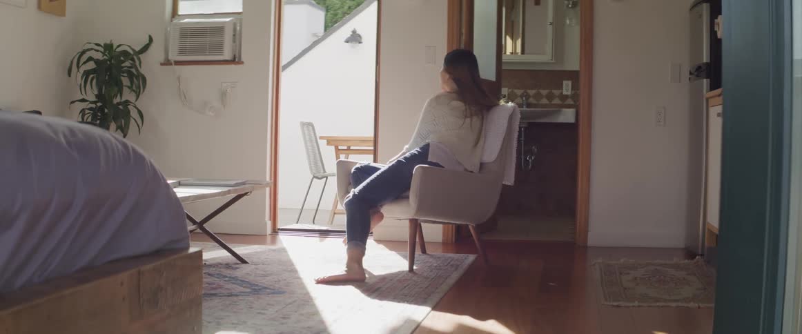 Asian woman with a white dress and jeans sits in an armchair and looks out the door