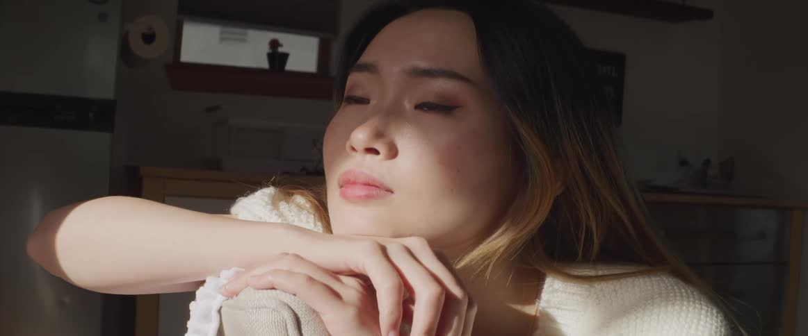 Asian woman with brown straight hair and a white sweater sits in an armchair in the living room