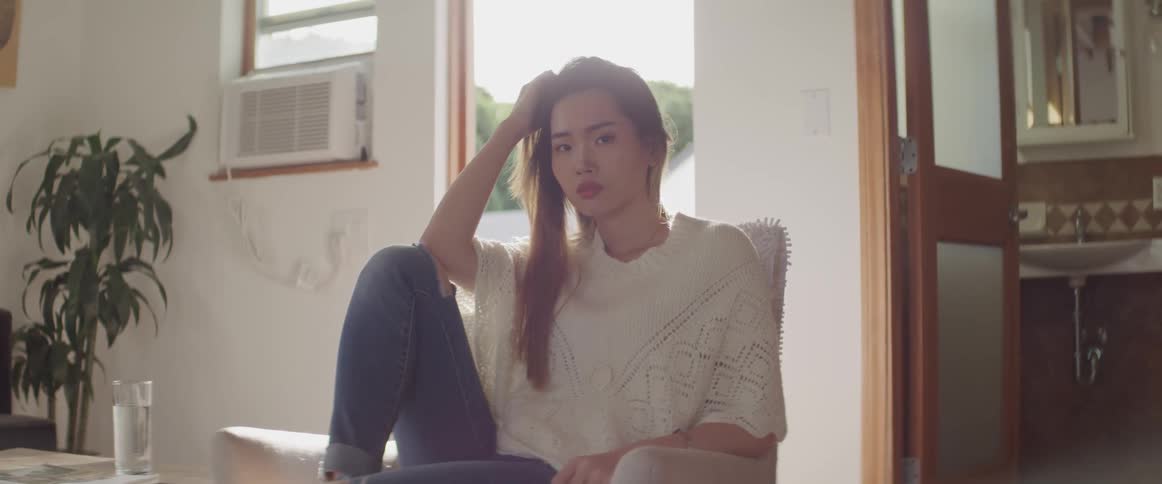 A young woman sitting at home runs her fingers through her hair as she sits in a chair
