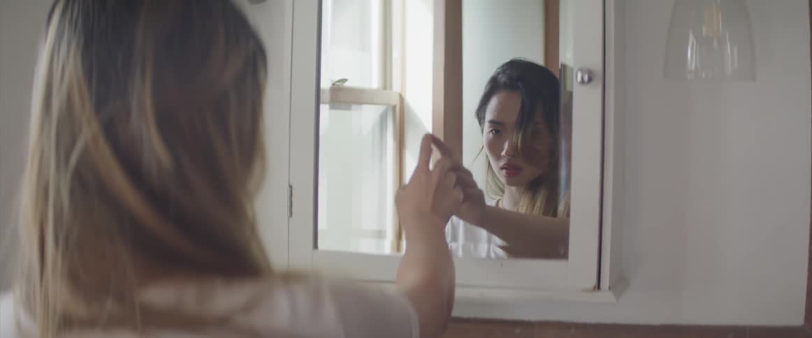 A woman is in a bathroom staring into a mirror and touching it